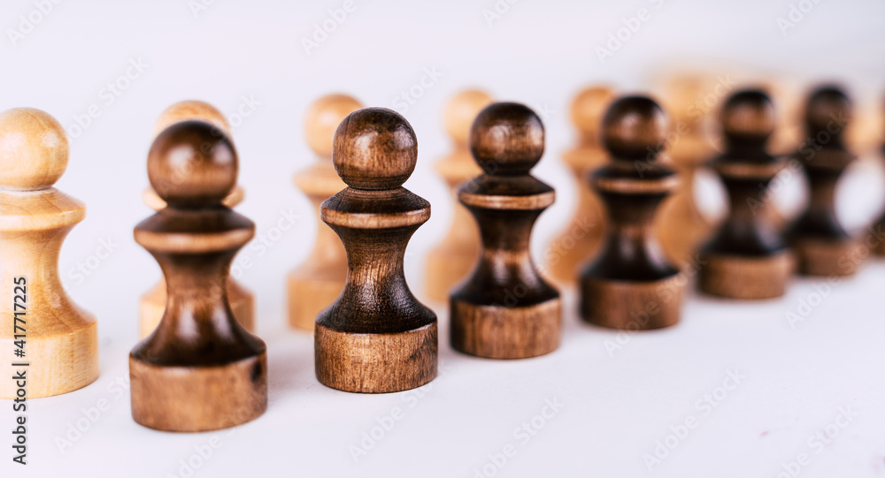 Close up of rows of black and white wooden chess pieces on white background. Selective focus on black pawns. Close up of rows of black and white wooden chess pieces on white background. Selective focus on black pawns.