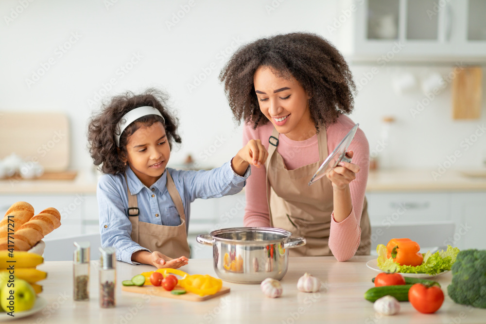 African american mom teaching daughter how to prepare soup
