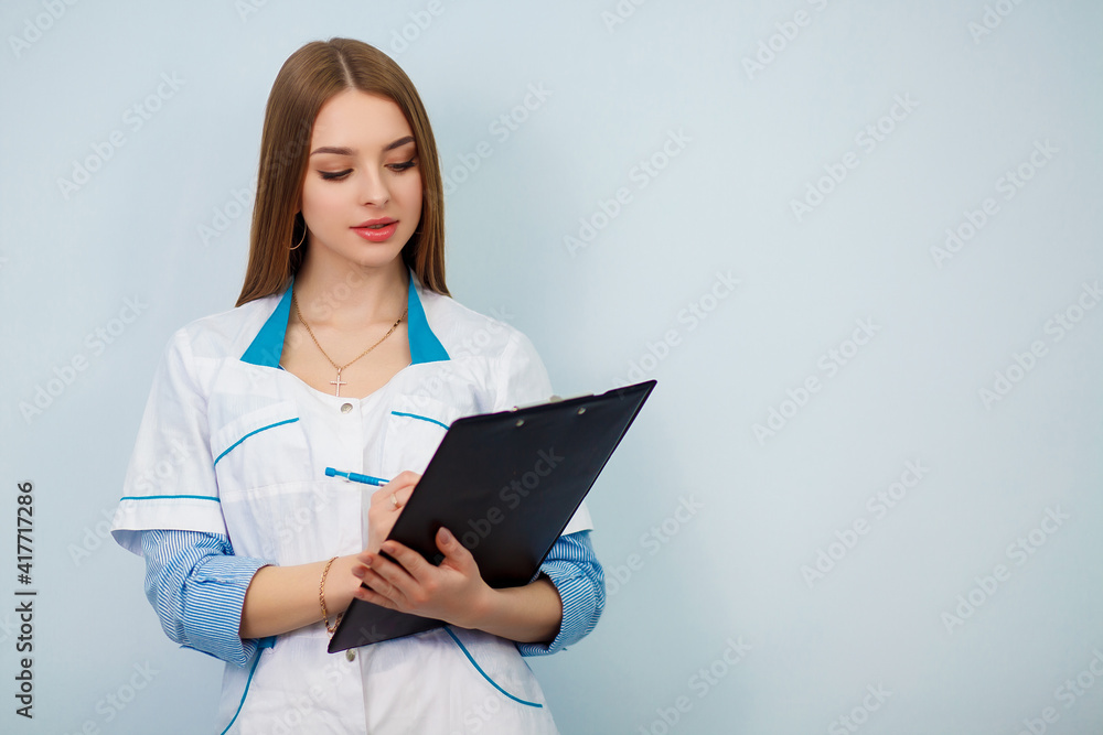 Photo of a young woman doctor posing isolated over white wall background holding clipboard. Health care concept. Beautiful girl in a white coat. Copy space. Photo of a young woman doctor posing isolated over white wall background holding clipboard. Health care concept. Beautiful girl in a white coat. Copy space.