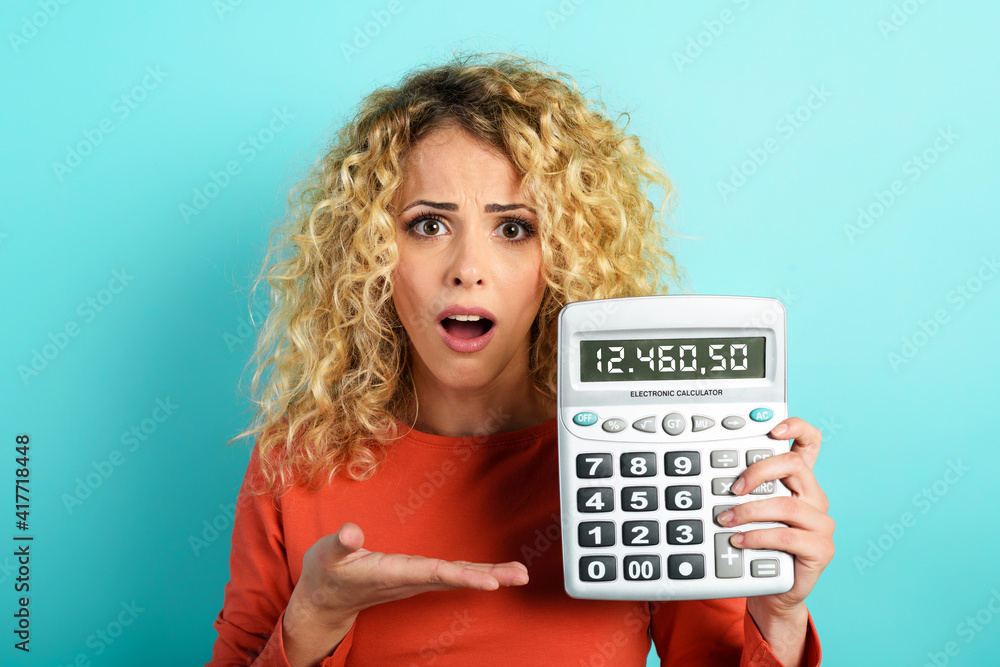 Girl is shocked and shows her debt on calculator display. Cyan background Girl is shocked and shows her debt on calculator display. Cyan background