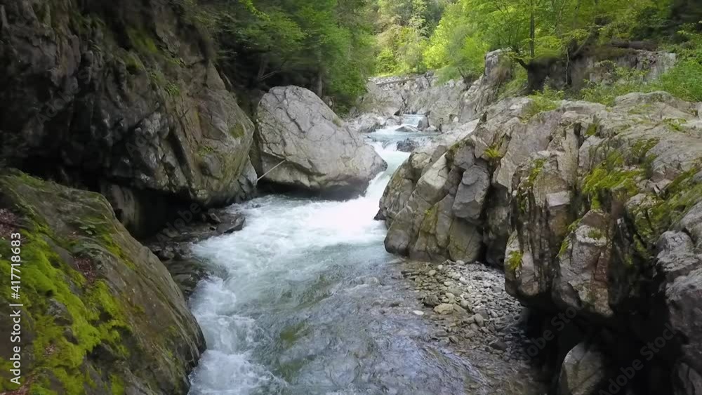 Aerial drone filming a rapid mountain river that flows through a narrow calcareous canyon. The valley crosses wild beech forests. Parang Mountains, Carpathia, Romania. Aerial drone filming a rapid mountain river that flows through a narrow calcareous canyon. The valley crosses wild beech forests. Parang Mountains, Carpathia, Romania.