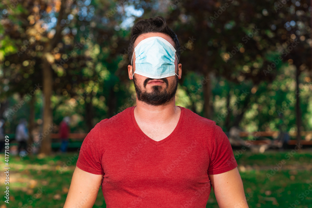 A shallow focus of a young man with crossed arms and a face mask on his eyes outdoors A shallow focus of a young man with crossed arms and a face mask on his eyes outdoors