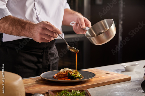 Cook in apron adding some sauce to dish. Cropped chef preparing food, meal, in kitchen, chef cooking, Chef decorating dish, closeup photo