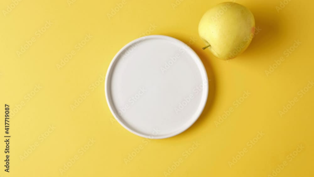 red yellow ripe apple rolls around a white plate on a yellow background top view. stop motion video red yellow ripe apple rolls around a white plate on a yellow background top view. stop motion video
