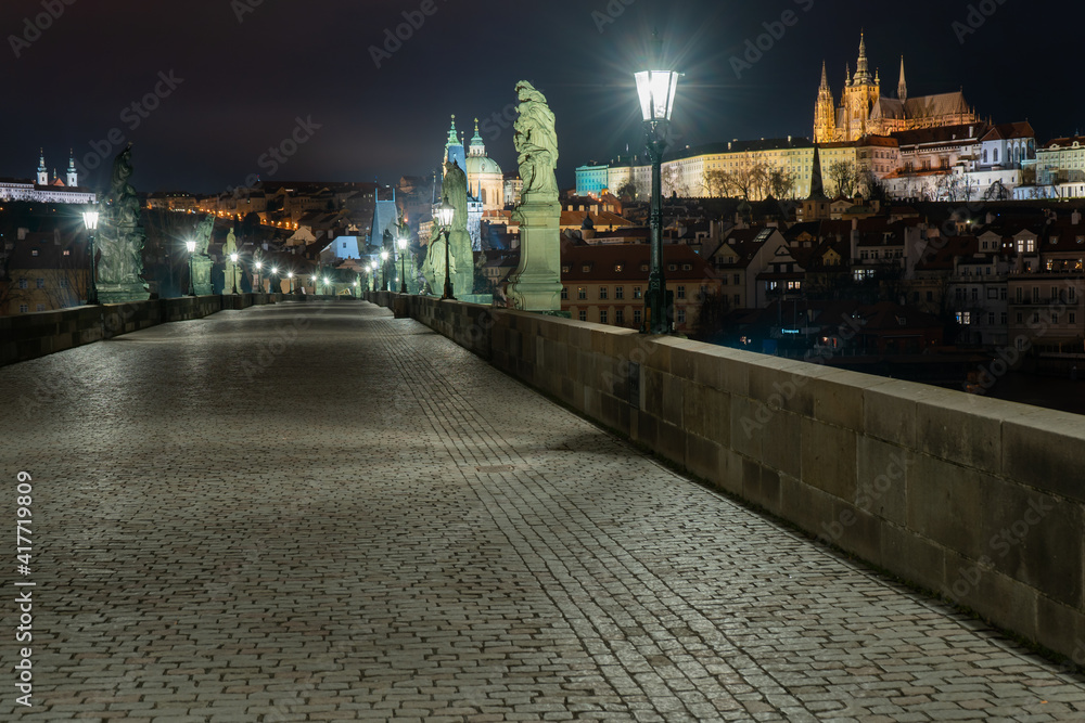 Fototapeta premium view of statues on Charles Bridge originally from the 17th century and light from lanterns and in the background Prague Castle and St. Vitus Cathedral in the center of Prague at night