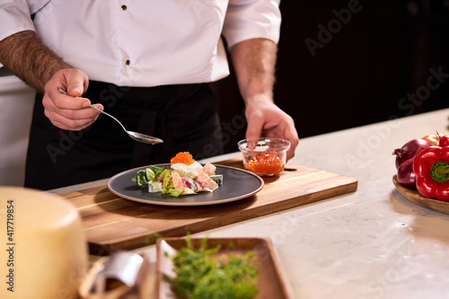 professional cook adds red caviar for salad, making tasty food in restaurant, master class of cooking. close-up photo