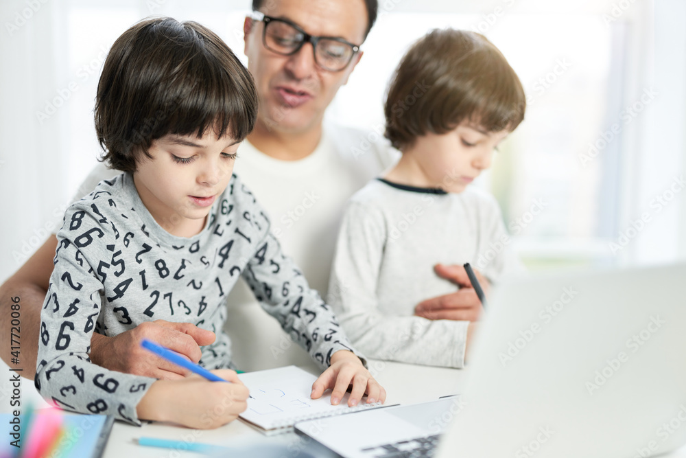 Teach your child. Cute little latin boy drawing while spending time with his dad and brother at home. Businessman using laptop while working from home and watching children Teach your child. Cute little latin boy drawing while spending time with his dad and brother at home. Businessman using laptop while working from home and watching children