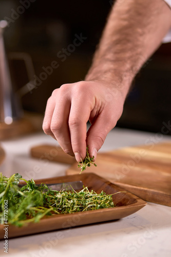 Close-up Male Chef Hands Taking Greens For Finishing Dish, Cropped Cook Adding Little Spice To Meal. In Restaurant or Cafe.