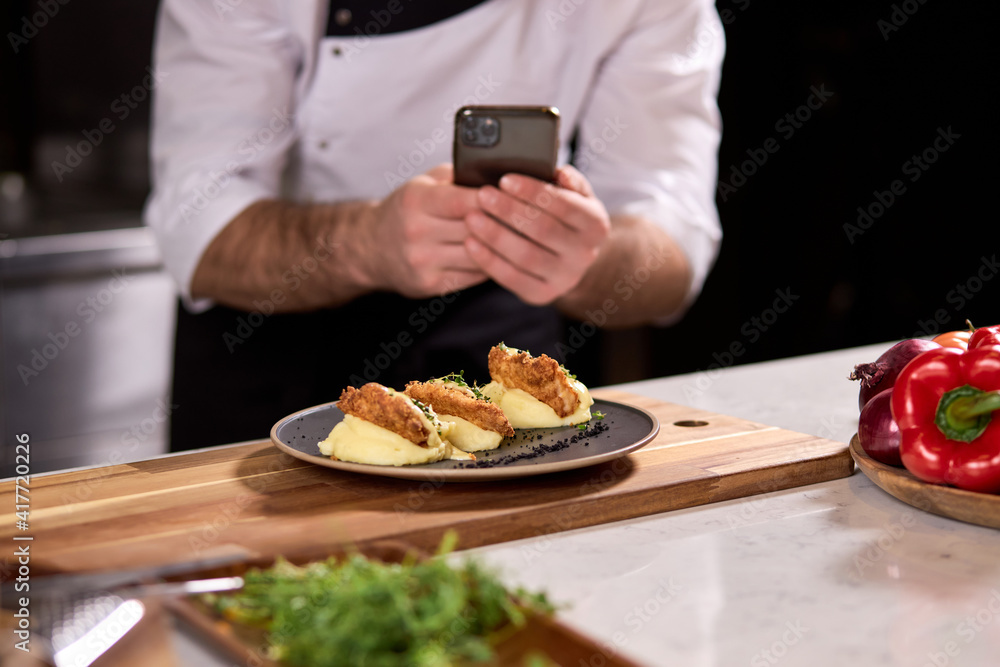 Cropped Chef Cook Take photo of Dish prepared by him, using smartphone. tasty yummy meal on plate is going to be served for restaurant guests Cropped Chef Cook Take photo of Dish prepared by him, using smartphone. tasty yummy meal on plate is going to be served for restaurant guests