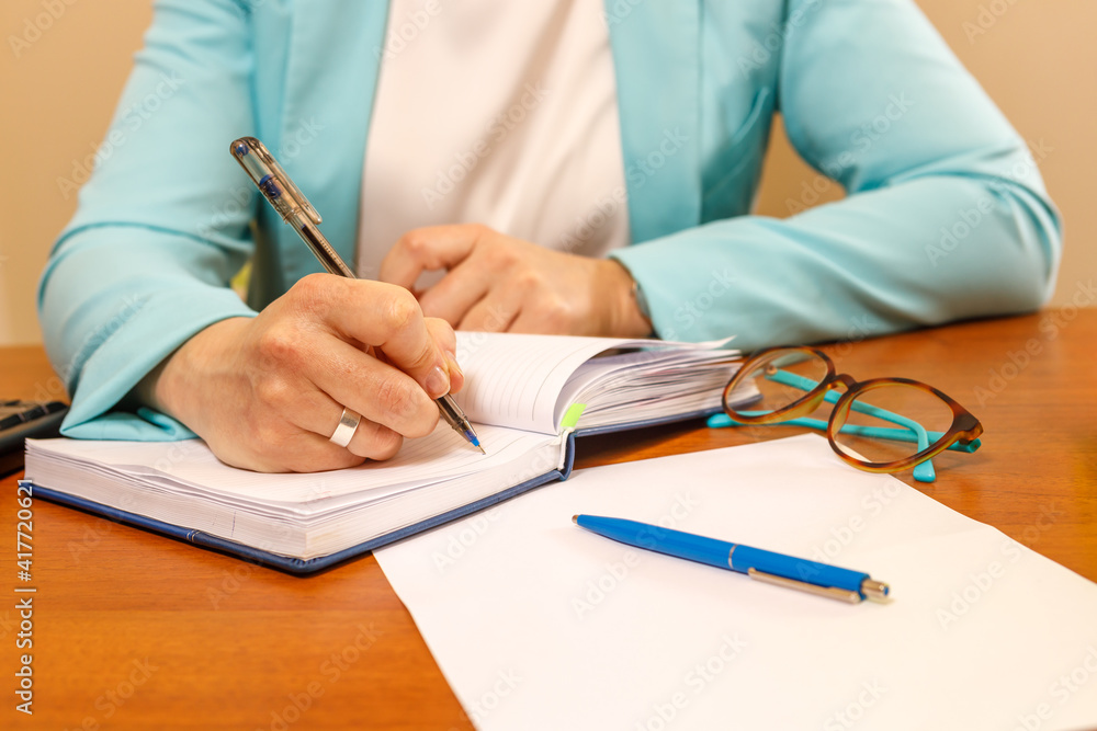 A businesswoman writes in her notebook while sitting at her desk. A businesswoman writes in her notebook while sitting at her desk.