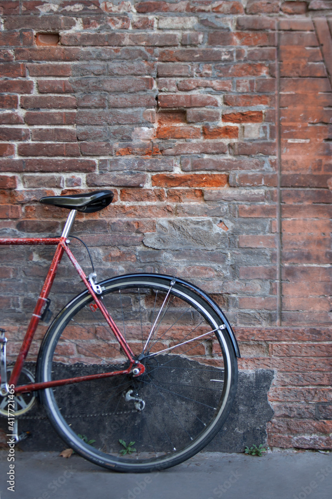 Abandoned bicycle leaning on the outside red brick wall. Bike tires. No people around.