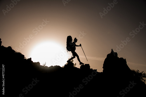 awesome view of female silhouette with tourist equipment walking along rocky path against sun © fesenko