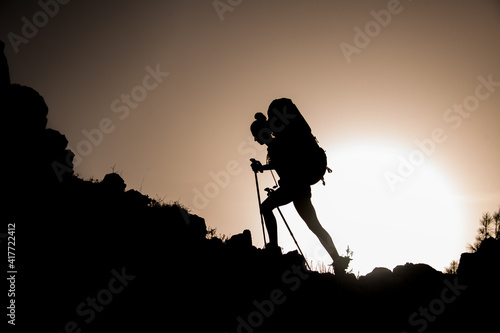 silhouette of woman tourist with trekking sticks and backpack who walks along rocky path