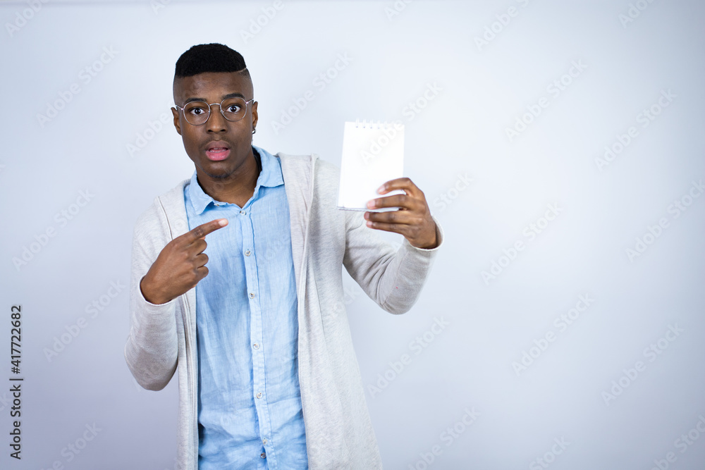 Young handsome african american man wearing casual clothes smiling and showing blank notebook Young handsome african american man wearing casual clothes smiling and showing blank notebook