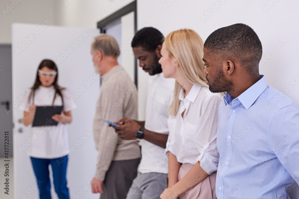 Head physician calls patients according to list to office, diverse men and women stand in row using smartphone, waiting in line. medicine concept. focus on african guy patient Head physician calls patients according to list to office, diverse men and women stand in row using smartphone, waiting in line. medicine concept. focus on african guy patient