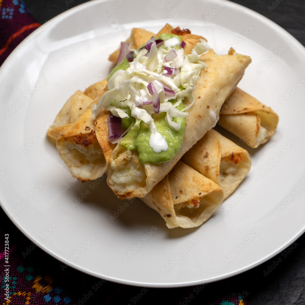 Fried tacos called flautas with guacamole and cabbage on dark background. Mexican food Fried tacos called flautas with guacamole and cabbage on dark background. Mexican food