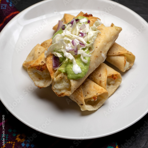 Fried tacos called flautas with guacamole and cabbage on dark background. Mexican food
