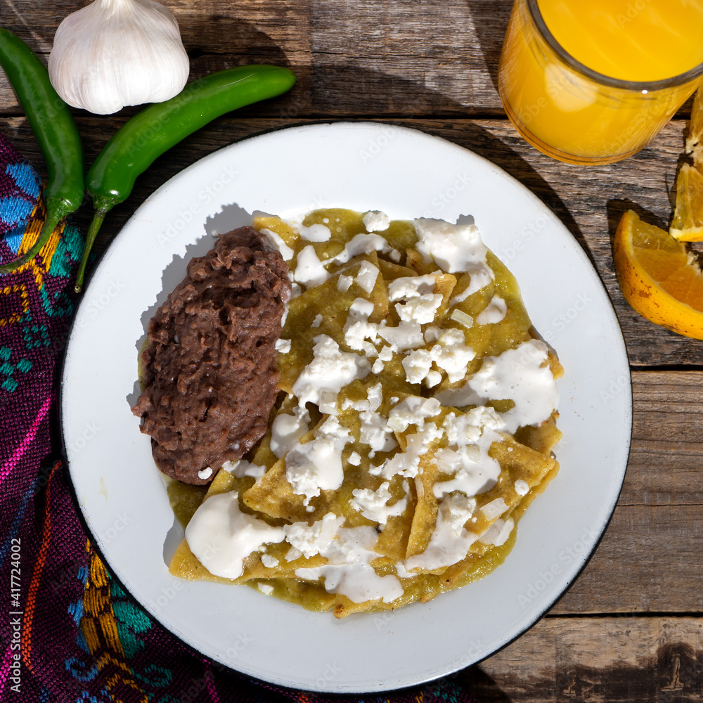 Green chilaquiles with refried beans and cheese on wooden background. Mexican food Green chilaquiles with refried beans and cheese on wooden background. Mexican food
