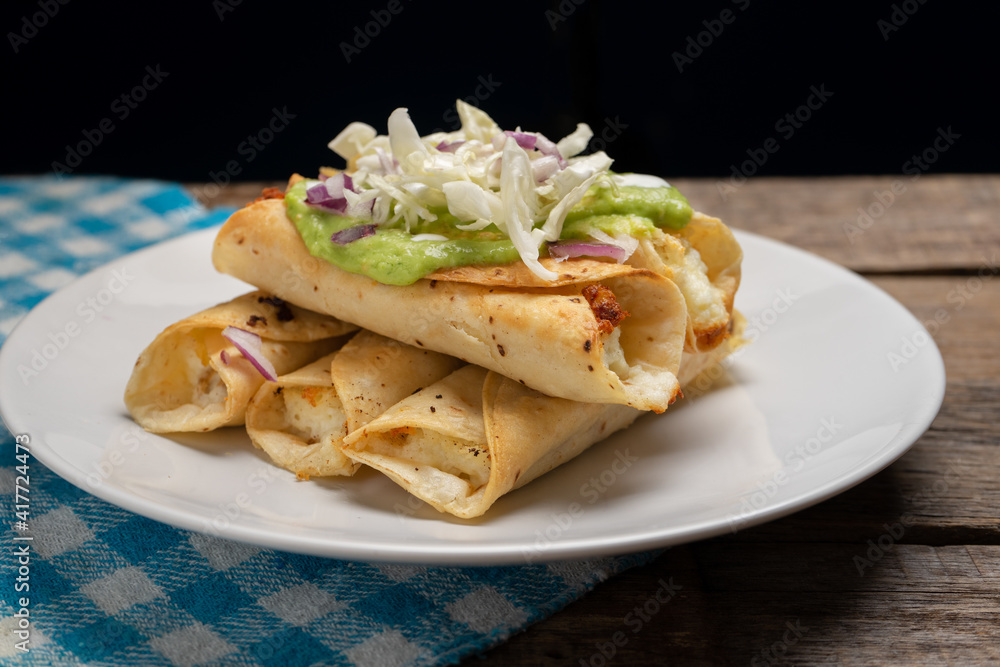 Fried tacos called flautas with guacamole and cabbage on wooden background. Mexican food