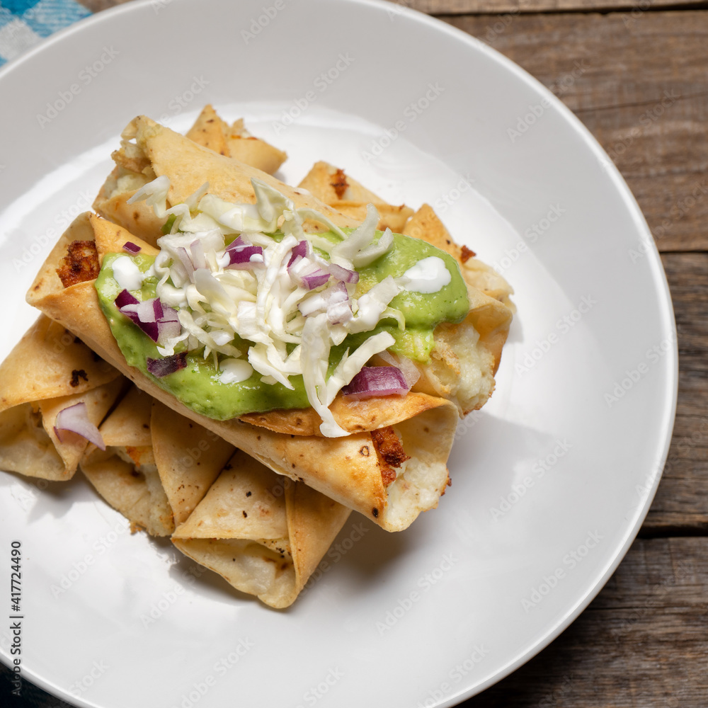 Fried tacos called flautas with guacamole and cabbage on wooden background. Mexican food Fried tacos called flautas with guacamole and cabbage on wooden background. Mexican food
