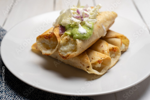 Fried tacos called flautas with guacamole and cabbage on white background. Mexican food