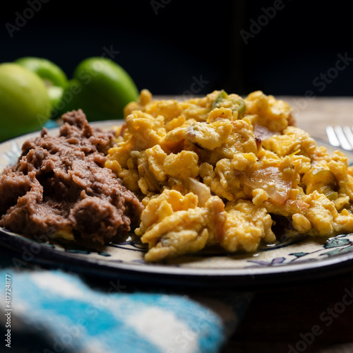 Scrambled eggs with green sauce and refried beans on wooden background. Mexican food