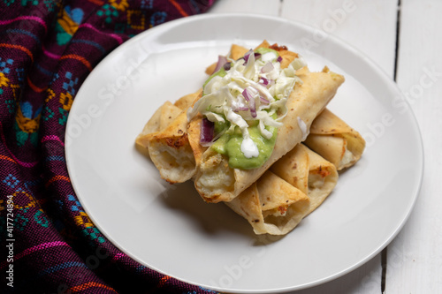 Fried tacos called flautas with guacamole and cabbage on white background. Mexican food © Guajillo studio