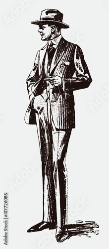 Standing fashionable older man from early 20th century with one hand in his trouser pocket, wearing suit and hat