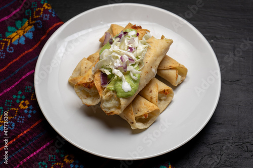 Fried tacos called flautas with guacamole and cabbage on dark background. Mexican food © Guajillo studio