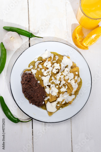 Green chilaquiles with refried beans and cheese on white background. Mexican food