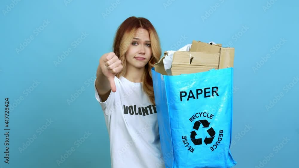 Teenager girl holding a recycling bag full of paper to recycle on back position looking back while scratching head over isolated background Teenager girl holding a recycling bag full of paper to recycle on back position looking back while scratching head over isolated background