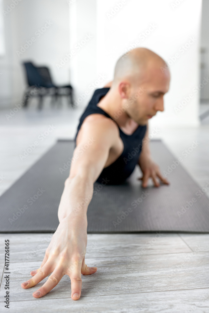 Athlete bald man stretching body on fitness mat holding hands on the floor, concentrated on workout alone in studio. focus on hand Athlete bald man stretching body on fitness mat holding hands on the floor, concentrated on workout alone in studio. focus on hand