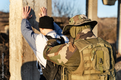 Back view of man in uniform unknown military soldier or special forces police arresting and searching criminal illegal migrant or terrorist in sunny day