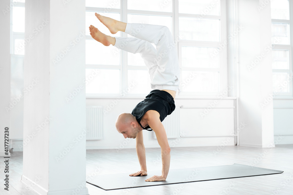 Experienced yogi man doing scorpion yoga pose in bright studio room. Caucasian male practicing yoga. Yogi concept. Side view. Experienced yogi man doing scorpion yoga pose in bright studio room. Caucasian male practicing yoga. Yogi concept. Side view.