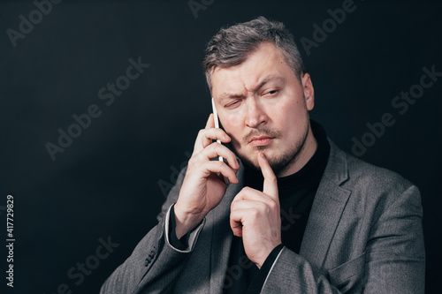 Man standing with hand on chin thinking about question during phone call, pensive expression. Thoughtful face. Doubt, hard decision, important information concept.