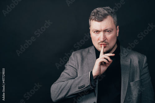 Confidential information, silence concept. Portrait of a serious business man showing silence gesture