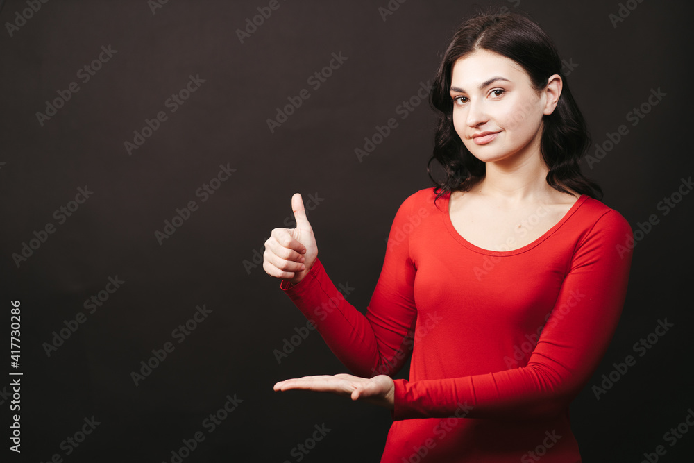 Presenting product, approve, admiration, special offer concept. Young woman with welcoming gesture and thumb up on black background, free space Presenting product, approve, admiration, special offer concept. Young woman with welcoming gesture and thumb up on black background, free space
