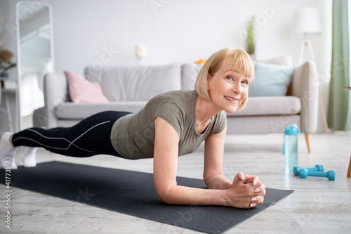 Home training concept. Smiling senior woman doing elbow plank on yoga mat in living room photo