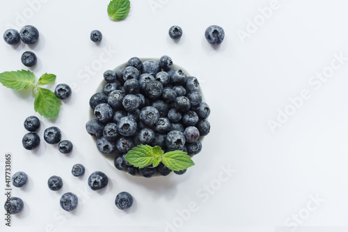 Fresh blueberries in white bowl and green leaves on white background. Flat lay, top view, copy space