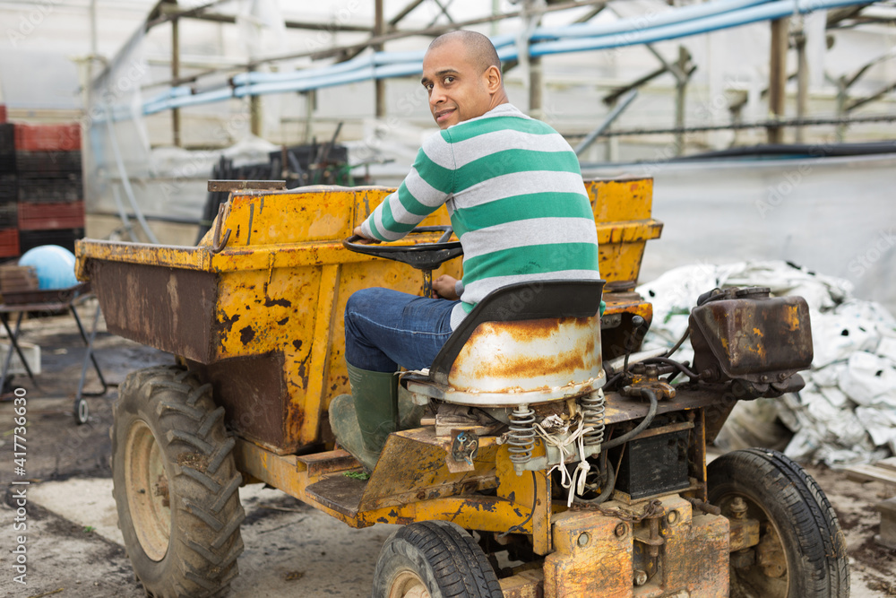 Middle aged hispanic man working on Forklift loader and removing garbage and dry grass from the territory at vegetable plant factory