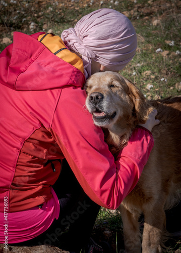 Woman with pink headscarf, affectionately hugging her dog and fighting cancer.