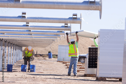 Two workers on construction site at solar farm lifting solar panel to install on metal tube structure