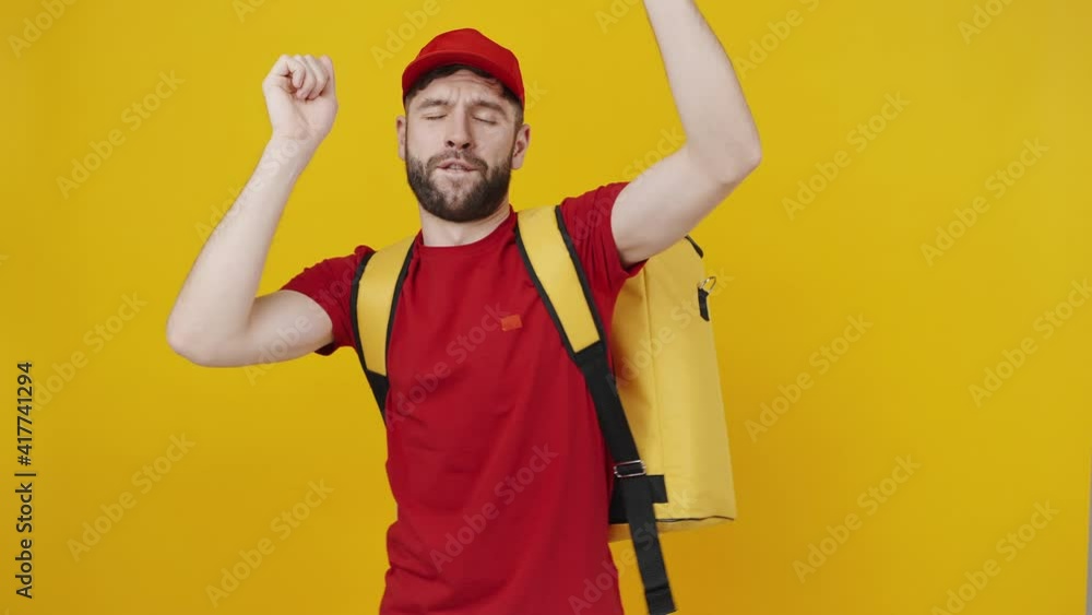 Young delivery man in uniform carrying thermo backpack dancing over orange studio background, smiling to camera Young delivery man in uniform carrying thermo backpack dancing over orange studio background, smiling to camera