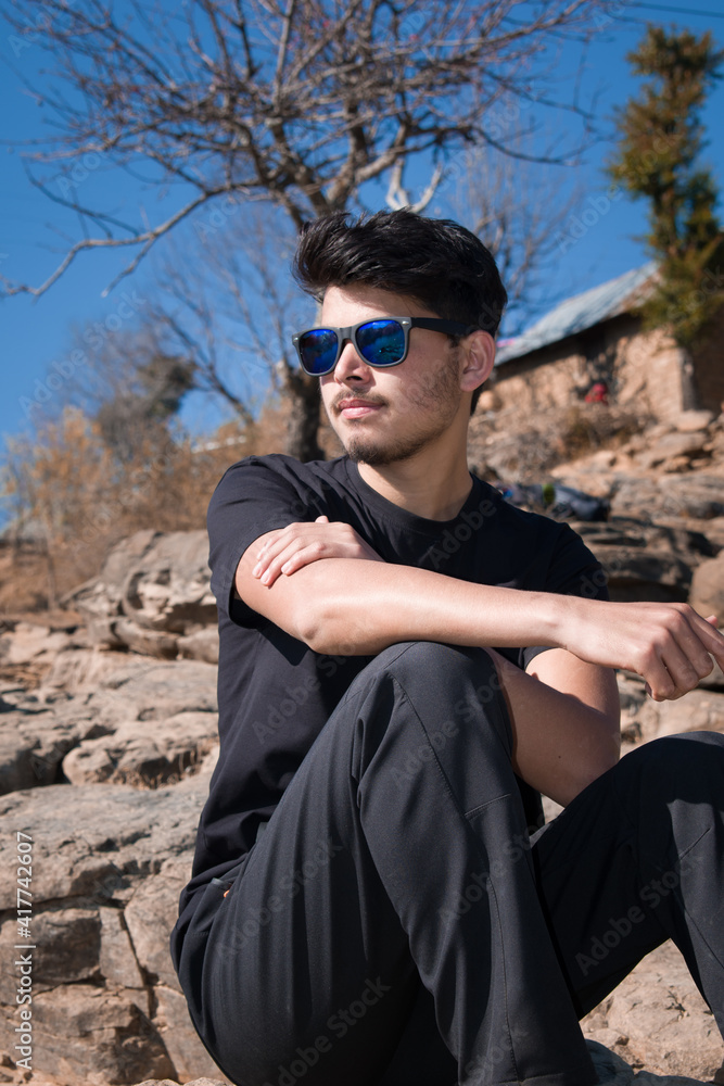 boy model sitting on rocks wearing black t-shirt black pant, sunglasses and looking away boy model sitting on rocks wearing black t-shirt black pant, sunglasses and looking away