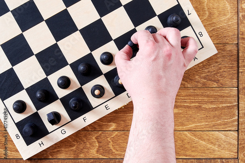 Fototapeta Naklejka Na Ścianę i Meble -  Mans hand take a black pawn to do a first chess move. Leisure activity and games