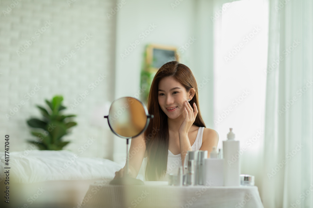 Happy Asian young woman smile and looking in mirror doing skin care touch cheek and beauty treatment at home,Wellness woman self care with beauty product at home Happy Asian young woman smile and looking in mirror doing skin care touch cheek and beauty treatment at home,Wellness woman self care with beauty product at home