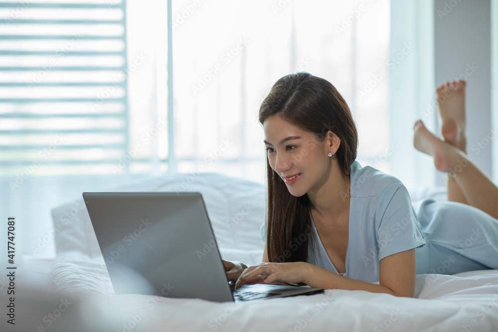Beautiful Attractive Asian young woman lying on bed and using computer laptop for using social media and shopping online relax in cozy bedroom in holiday,Lifestyle in home Concept Beautiful Attractive Asian young woman lying on bed and using computer laptop for using social media and shopping online relax in cozy bedroom in holiday,Lifestyle in home Concept