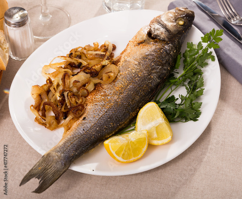 Whole oven baked sea bass fish with roasted onion on white plate photo