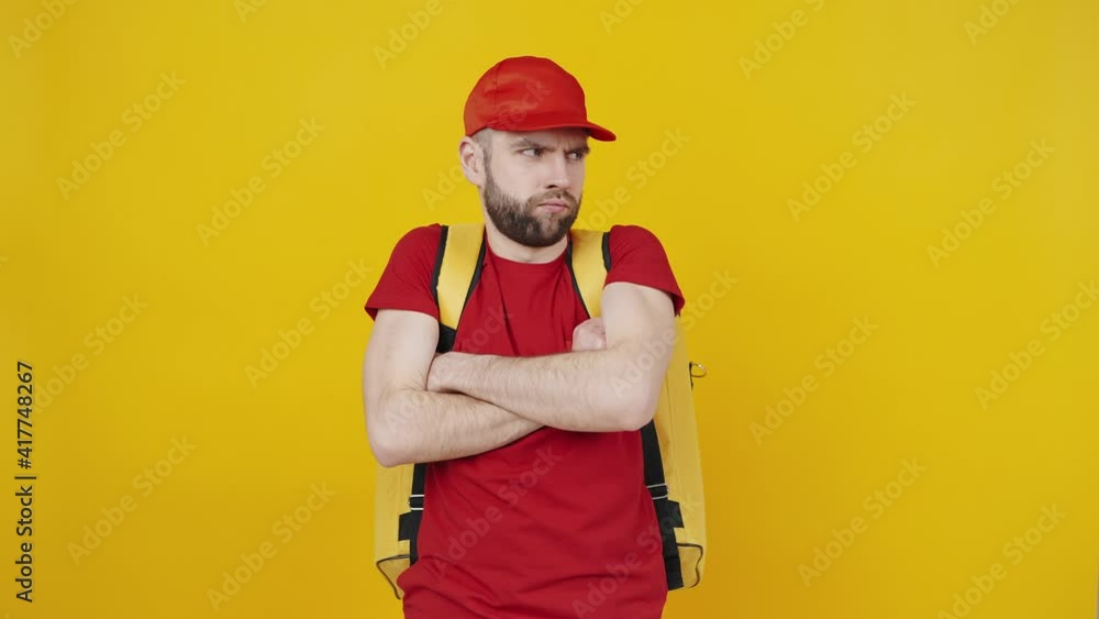 Thankless job. Young upset delivery man crossing hands and pouting lips, feeling offended, yellow background Thankless job. Young upset delivery man crossing hands and pouting lips, feeling offended, yellow background