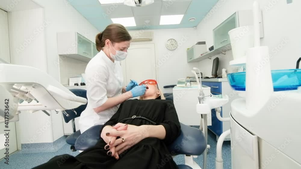 dentist holding dental instruments in the mouth of a woman client. The dentist holds the probe in one hand and the mouthpiece in the other. The doctor checks the condition of the teeth. cabinet dentist holding dental instruments in the mouth of a woman client. The dentist holds the probe in one hand and the mouthpiece in the other. The doctor checks the condition of the teeth. cabinet